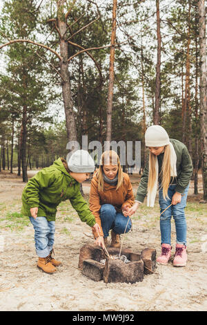 Felice giovane madre e bambini facendo falò in pineta Foto Stock