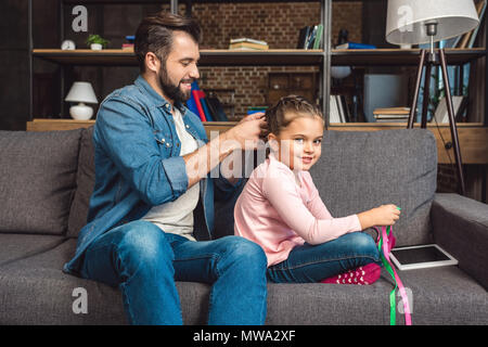 Padre rendendo la treccia di capelli per la figlia comodamente seduti sul divano di casa Foto Stock