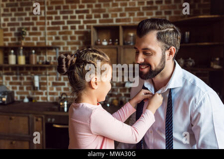 Piccola figlia abbottonatura shirt per padre su cucina Foto Stock