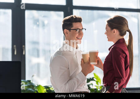 Felice colleghi con bicchieri di carta di caffè a parlare e flirtare Foto Stock