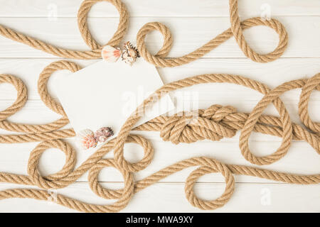 Vista superiore della carta vuoti con conchiglie su marrone Nautica Corde annodate su bianco superficie in legno