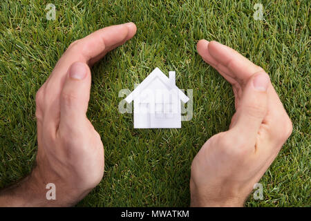 Vista in elevazione di una mano umana proteggere casa modello su erba verde Foto Stock