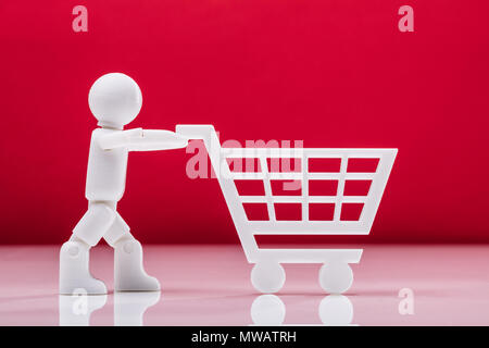 Vista laterale di una figura umana che trasportano Shopping Card contro lo sfondo rosso Foto Stock