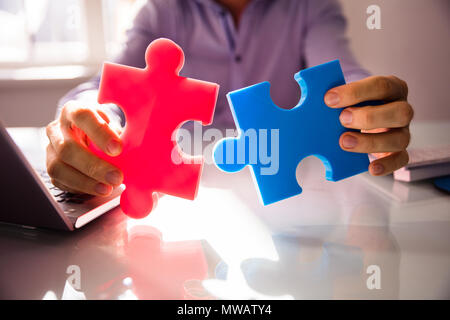 Close-up di commercianti la mano che regge due White Jigsaw Puzzle su scrivania Foto Stock