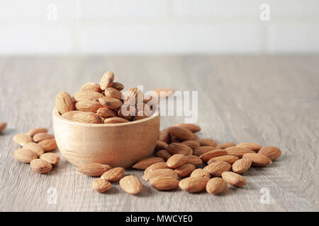 Semi di mandorle un overflow marrone ciotola di legno e il pavimento è sceso. Posto su una tavola di legno con copia spazio. Selezionare la messa a fuoco leggera profondità di campo e blurre Foto Stock