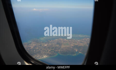 Vista attraverso un aereo finestra sull'isola tropicale, oceano e Cielo e nubi. Vista aerea del mare, le nuvole e il cielo come visto attraverso la finestra di un aeromobile. Concetto di viaggio. Foto Stock