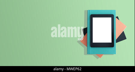 Vista dall'alto di e-book reader sulla pila di libri sul desktop verde Foto Stock