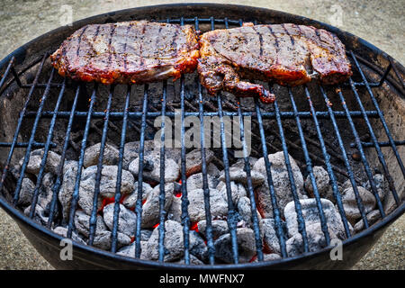 Due bistecche di carne stagionata seduto sopra la brace su un piccolo grill all'aperto. Foto Stock