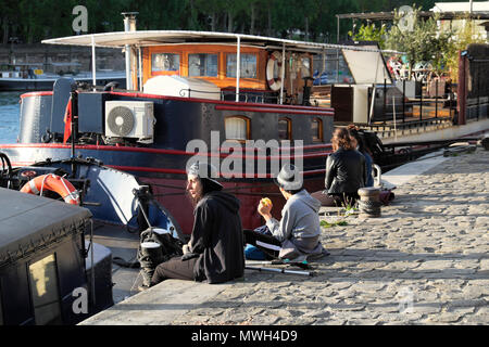 La gente seduta su un ciottolo quai da barche sulla riva sinistra lungo il Fiume Senna su una molla nel pomeriggio in aprile a Parigi, Francia KATHY DEWITT Foto Stock