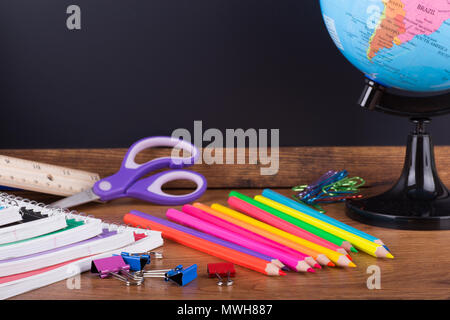 Assortimento di ritorno a scuola su un desktop di legno con una lavagna vuota in background Foto Stock