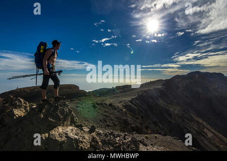 Uomo con zaino in piedi sulla roccia vicino al teide cercando su sun su Tenerife Foto Stock