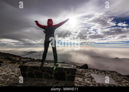 Uomo che salta da banco con le mani in alto di fronte sun con le nuvole in cielo e sulle colline Foto Stock