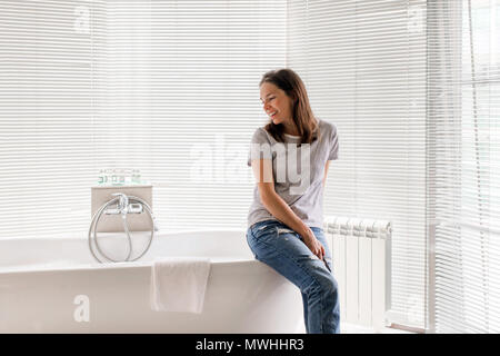 Donna sorridente seduta sulla vasca da bagno Foto Stock