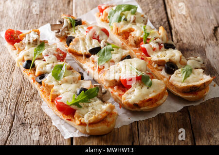 Hot gustoso taglio baguette cotta con pollo, formaggio, pomodori, olive e funghi vicino sul tavolo orizzontale. Foto Stock