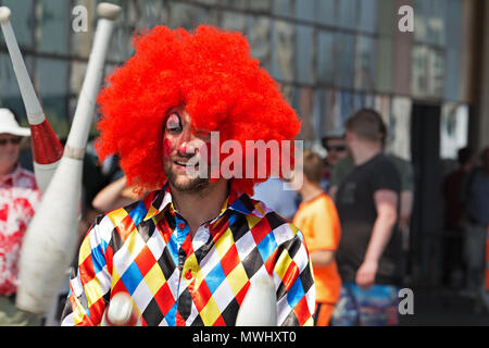 Un animatore di strada vestito come un clown intrattiene la folla con un po' di giocoleria Foto Stock