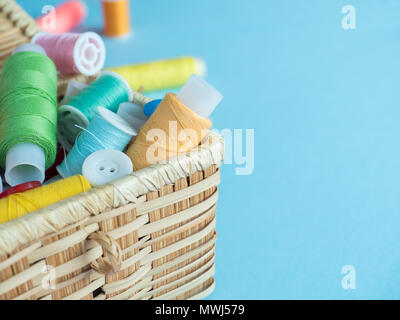 Colorati pulsanti di cucitura e thread in una scatola di legno su uno sfondo blu Foto Stock