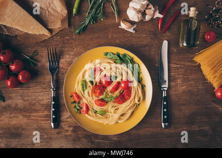 Lay piatto con i tradizionali piatti di pasta italiana con pomodori e rucola in piastra su un tavolo di legno con ingredienti Foto Stock