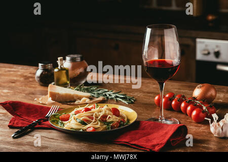 Tradizionale pasta italiana con pomodori e rucola in piastra e un bicchiere di vino rosso Foto Stock