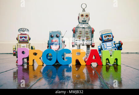 Il programma word con lettere in legno e retrò robot giocattolo su un vecchio pavimento in legno con la riflessione Foto Stock