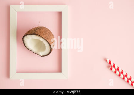 Mezza noce di cocco nel telaio bianco pastello contro sfondo rosa minimo concetto creativo. Spazio per la copia. Foto Stock