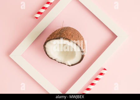Mezza noce di cocco nel telaio bianco pastello contro sfondo rosa minimo concetto creativo. Foto Stock