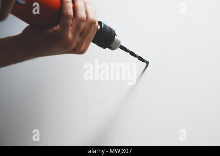 La perforazione nella parete. L'uomo è in possesso di un cacciavite o un trapano a mano. Le punte di un foro nella parete utilizzando un trapano con una punta da trapano. Concetto di faccende domestiche, r Foto Stock