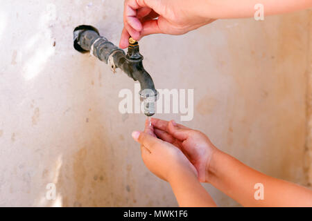 Donna aprire a mano il rubinetto dell'acqua e il bambino lavarsi le mani. Close-up. Foto Stock