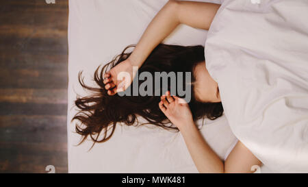 Vista dall'alto di una donna che dorme sul letto che copre il volto. In prossimità di una donna in un profondo sonno con la sua mano accanto alla sua testa e capelli let loose. Foto Stock