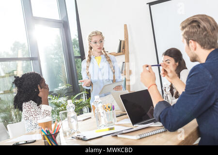 Gruppo multiculturale della gente di affari a discutere di lavorare mentre si è seduti al posto di lavoro in ufficio Foto Stock