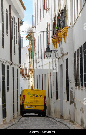 Giallo van spreme attraverso la stretta viuzza acciottolata a Cordoba, Spagna. Tradizionali pareti dipinte di bianco, un vecchio lampione in metallo, giallo scatole di finestra. Foto Stock