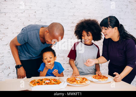 La famiglia felice di African American genitori e piccolo ragazzo e ragazza avente la pizza insieme felicemente a casa. La famiglia e la genitorialità concept Foto Stock