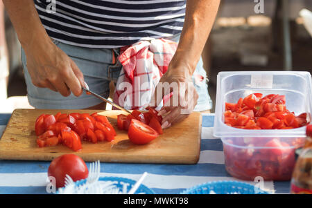 La donna le mani per affettare il pomodoro rosso sul tagliere di legno. Lo Chef costolette di mele paradiso per un insalata di verdure. Street food festival. Insalata di organico. Foto Stock