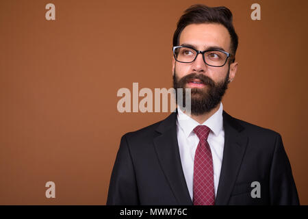 Giovane bello barbuto imprenditore persiano contro backgro marrone Foto Stock