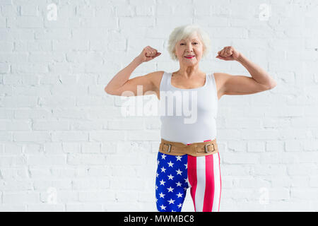 Felice senior sportive che mostra i muscoli e sorridente in telecamera Foto Stock