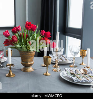 Vista ravvicinata del bouquet di tulipani rossi sul piano portapaziente con disposti vintage posate e candele Foto Stock