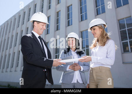 Il team professionale di architetti sorridente blueprint di contenimento mentre in piedi insieme Foto Stock