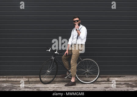 Elegante uomo in occhiali da sole il fumo di sigarette e di seduta in bicicletta Foto Stock