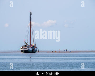 Un gruppo di ragazzi giocare sulla sabbia piatta e asciugata a fondo piatto yacht a vela a bassa marea sul mare di Wadden, Paesi Bassi Foto Stock