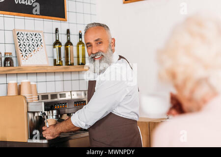 Messa a fuoco selettiva di sorridere senior barista il caffè nella caffetteria Foto Stock