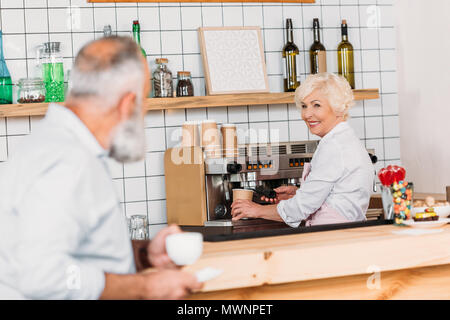 Messa a fuoco selettiva di sorridere senior barista con macchina per il caffè mentre il caffè nella caffetteria Foto Stock