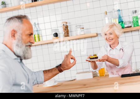 Messa a fuoco selettiva di sorridere cafe lavoratore offrendo pasticceria a senior man a contatore Foto Stock