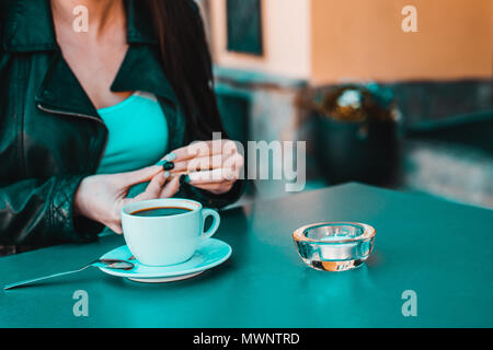 Una donna si rilassa al caffè. Sul tavolo si trova un bianco tazza di caffè, sullo sfondo di una donna contiene zucchero nella sua mano. Stile di vita. Foto Stock