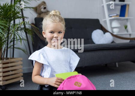 Adorable Little Schoolgirl con zaino la preparazione per la scuola e sorridente in telecamera Foto Stock