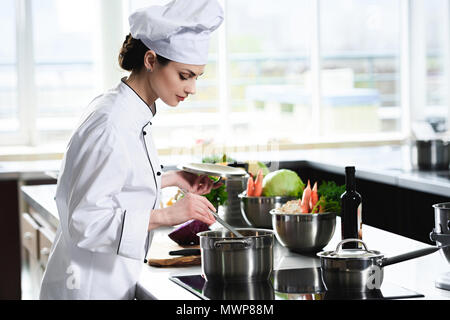 Donna chef cucinare in padella sul fornello da cucina Foto Stock