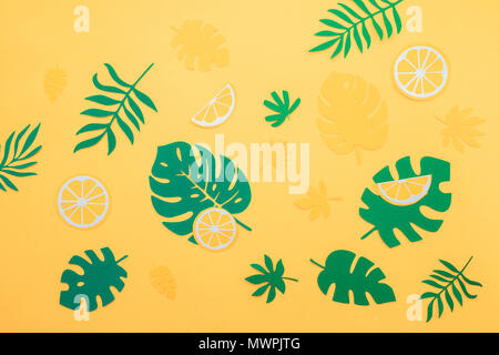 Foglie tropicali pattern. Green monstera e foglie di felce con fette di arancia e limone su un brillante sfondo giallo. La vacanza estiva concetto con carta artigianale di frutta Foto Stock