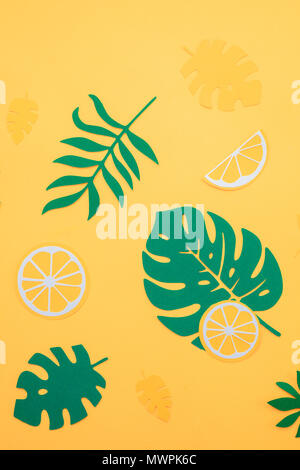 Foglie tropicali pattern. Green monstera e foglie di felce con fette di arancia e limone su un brillante sfondo giallo. La vacanza estiva concetto con carta artigianale di frutta Foto Stock