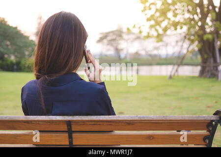 Vista posteriore della donna a parlare su un telefono su una panchina nel parco pubblico Foto Stock