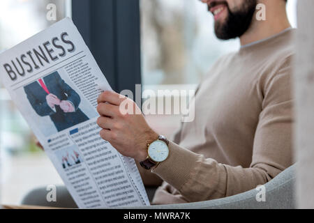 Immagine ritagliata di imprenditore sorridente in seduta cafe e il giornale di lettura Foto Stock