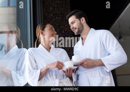 Matura in accappatoi holding tazze di tè e sorridente ogni altro nel centro spa Foto Stock