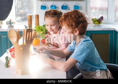 Dei bambini felici con tavoletta digitale mentre si cucina insieme in cucina Foto Stock